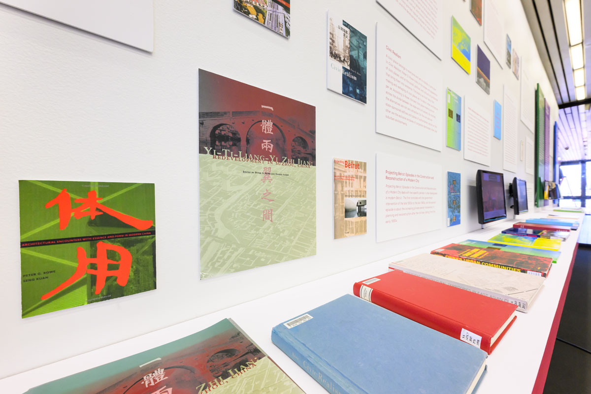 a detail view of long shelf of books on display in front of an exhibition wall of book covers and abstracts