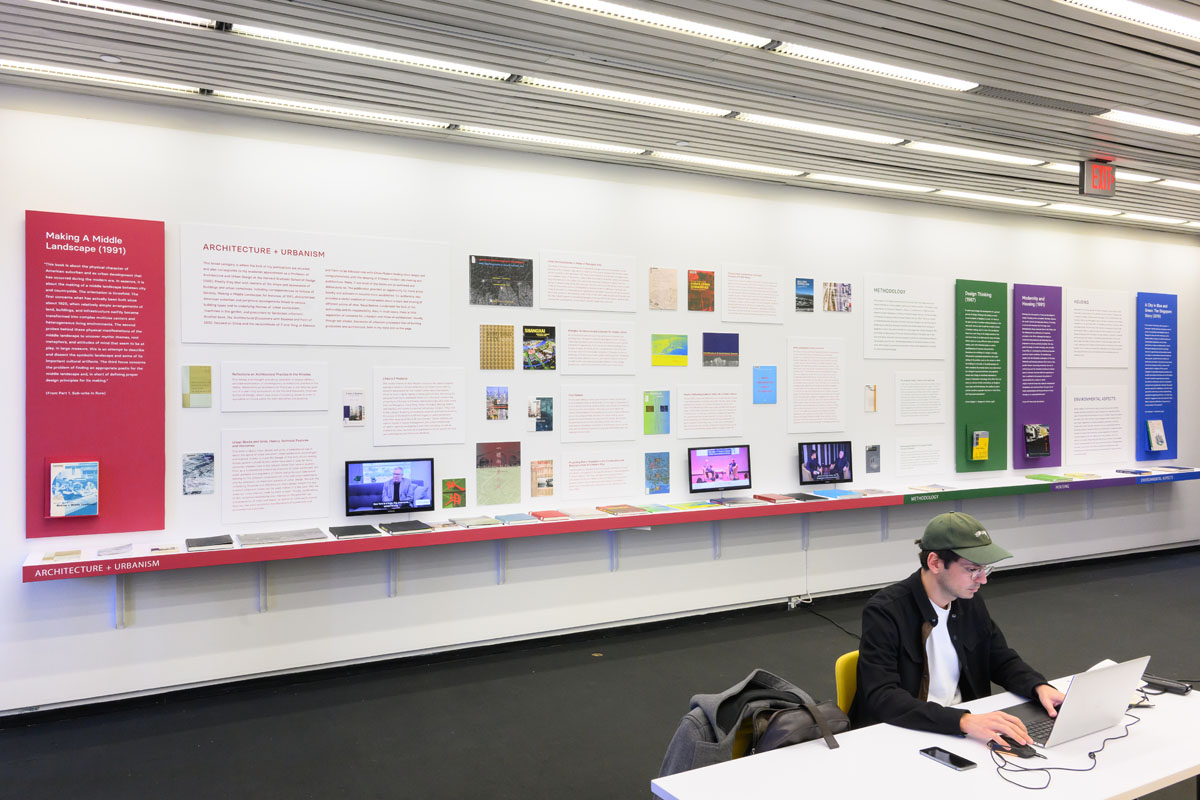 A long shelf of books on display in front of an exhibition wall of book covers and abstracts