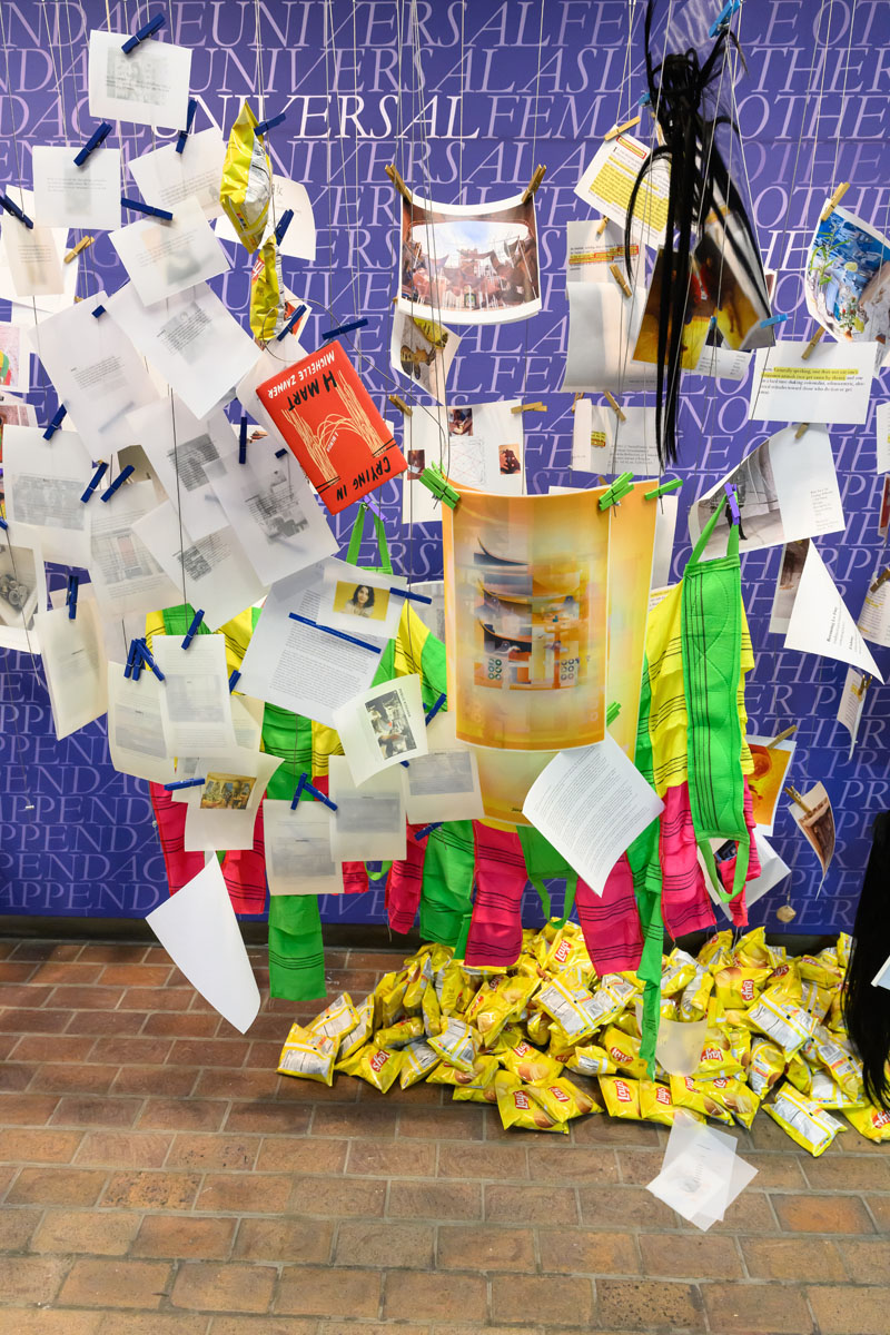 Printed images and text held onto wires with many colored clothes pins over a pile of potato chip bags on the floor