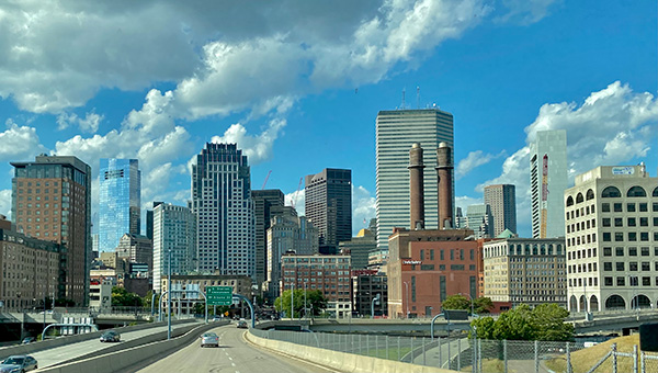 A photograph of the Boston skyline with a highway in the foreground and tall buildings dominating the view.