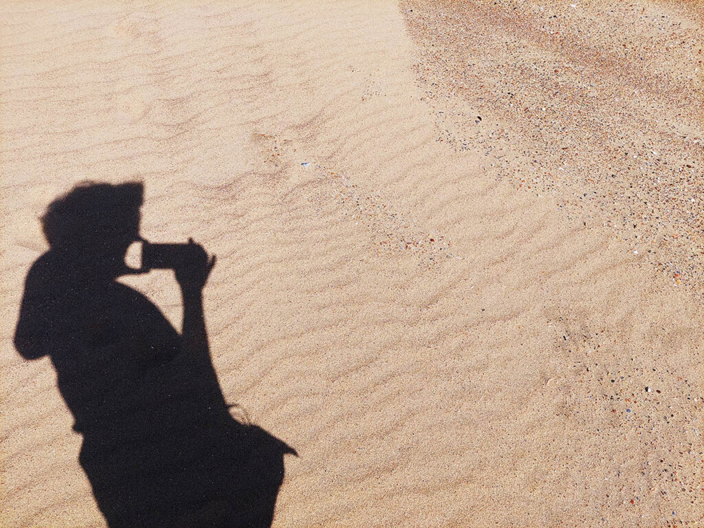The shadow of a person taking a photo cast on desert sand.