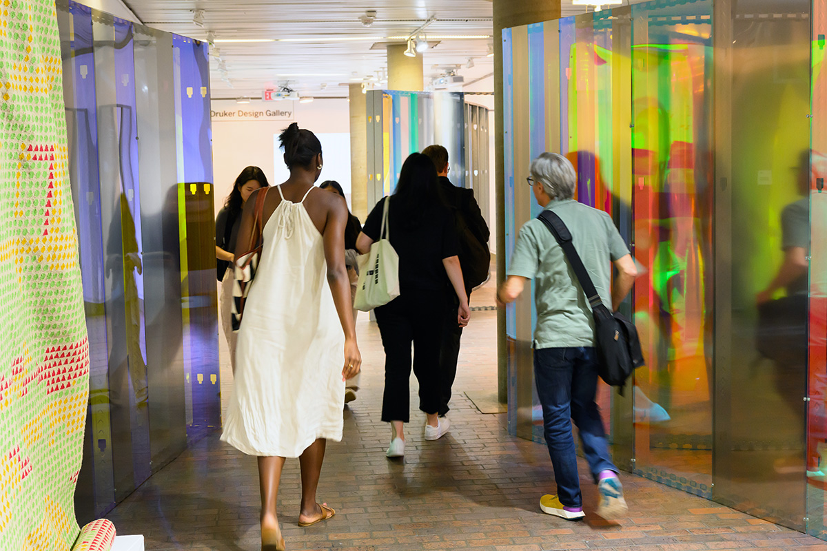 Multiple people walking through a reflective curved plexiglass structure inside Druker Design Gallery.