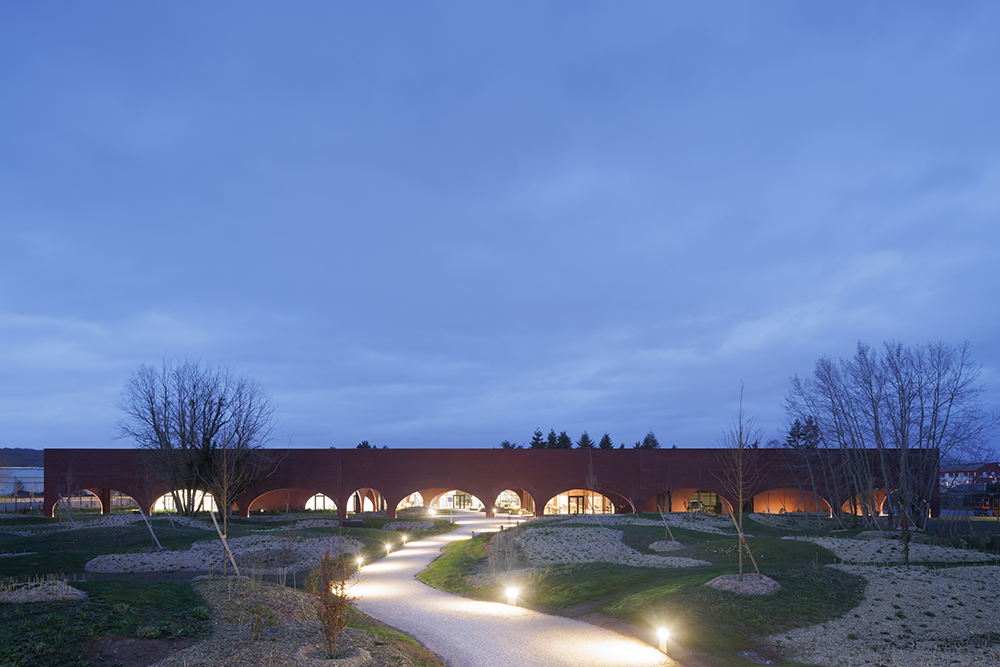 A low brick arched structure sits at the end of a winding path and is surrounded by a blue sky at dusk.