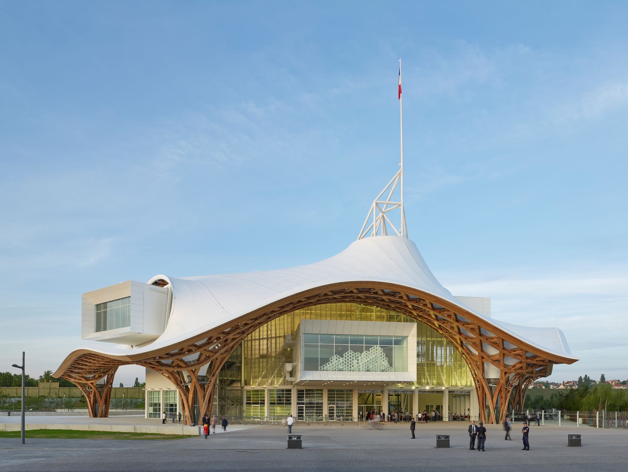 Building with curved white roof and people standing nearby. The sky is bright blue.