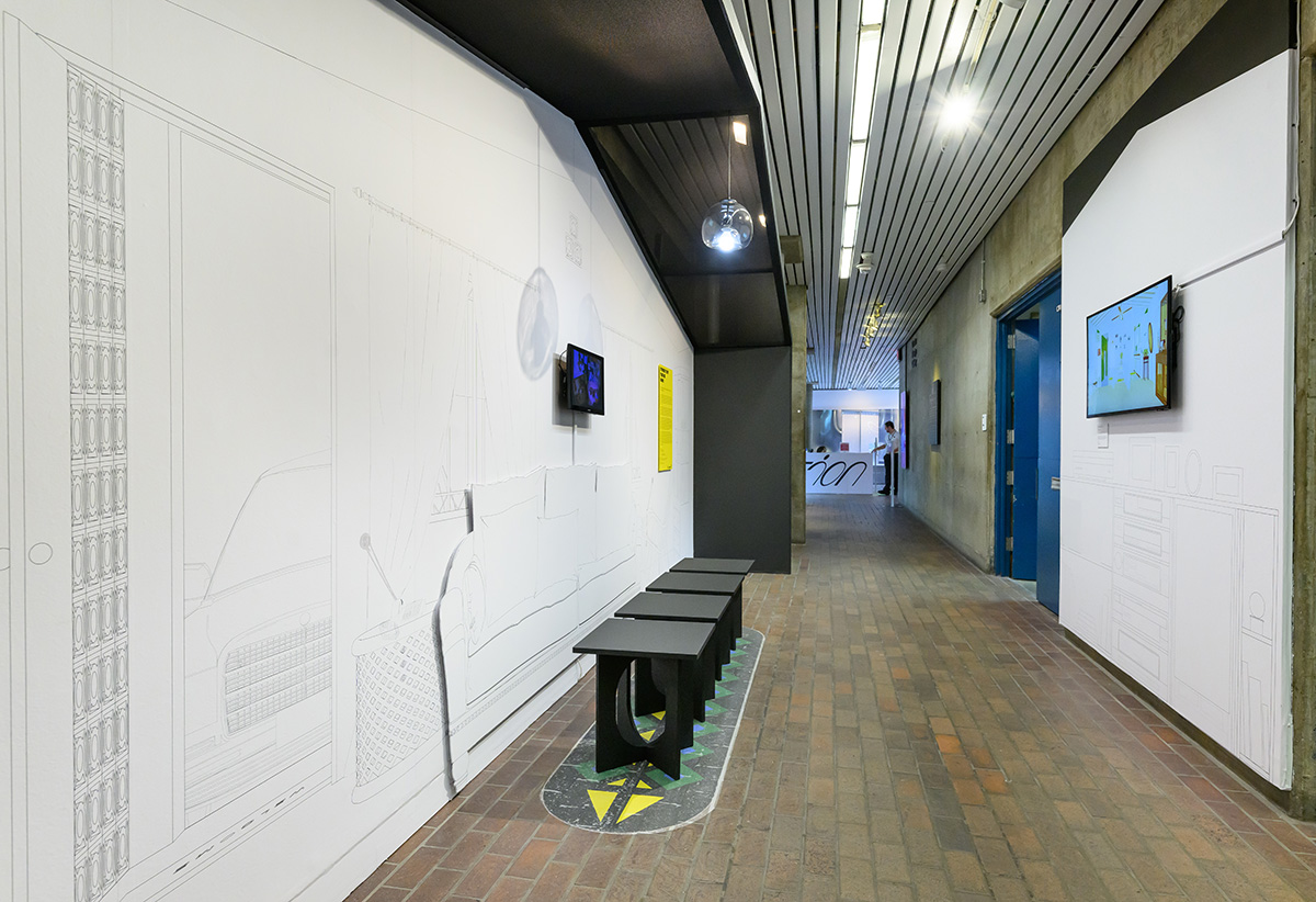 A view of the exhibit in Gund hall showing a group of four stools in front of a line drawing of a domestic living room with video screens on the walls and a roof structure overhead.