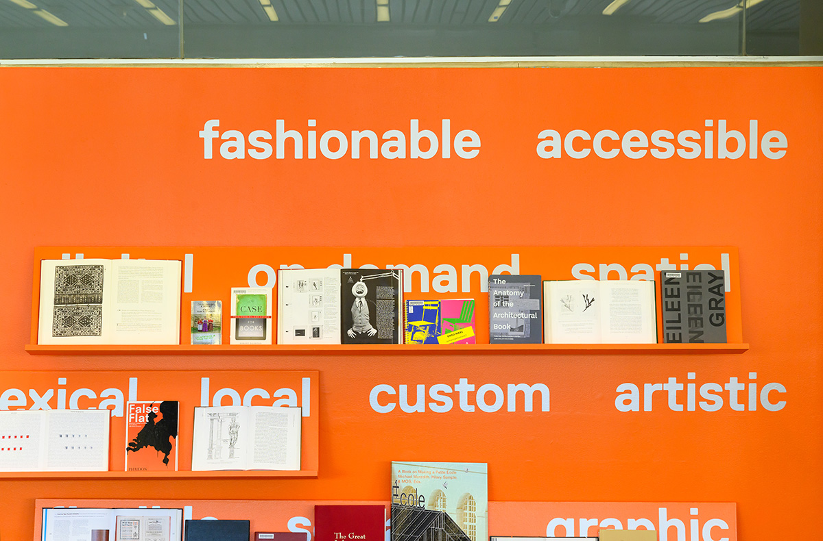 An orange wall with shelves of books on display.