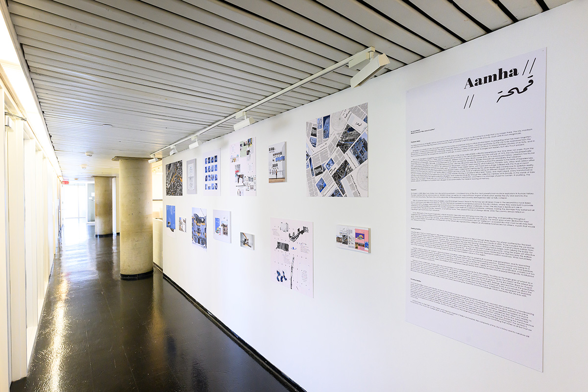 A view of a corridor in Gund Hall showing a white wall with images and a large panel of text under the heading “Aamha”