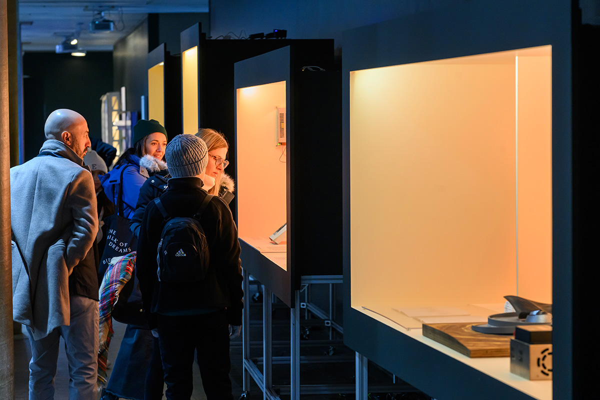 A group of people looking at items inside a lit display case inside Druker Design Gallery.