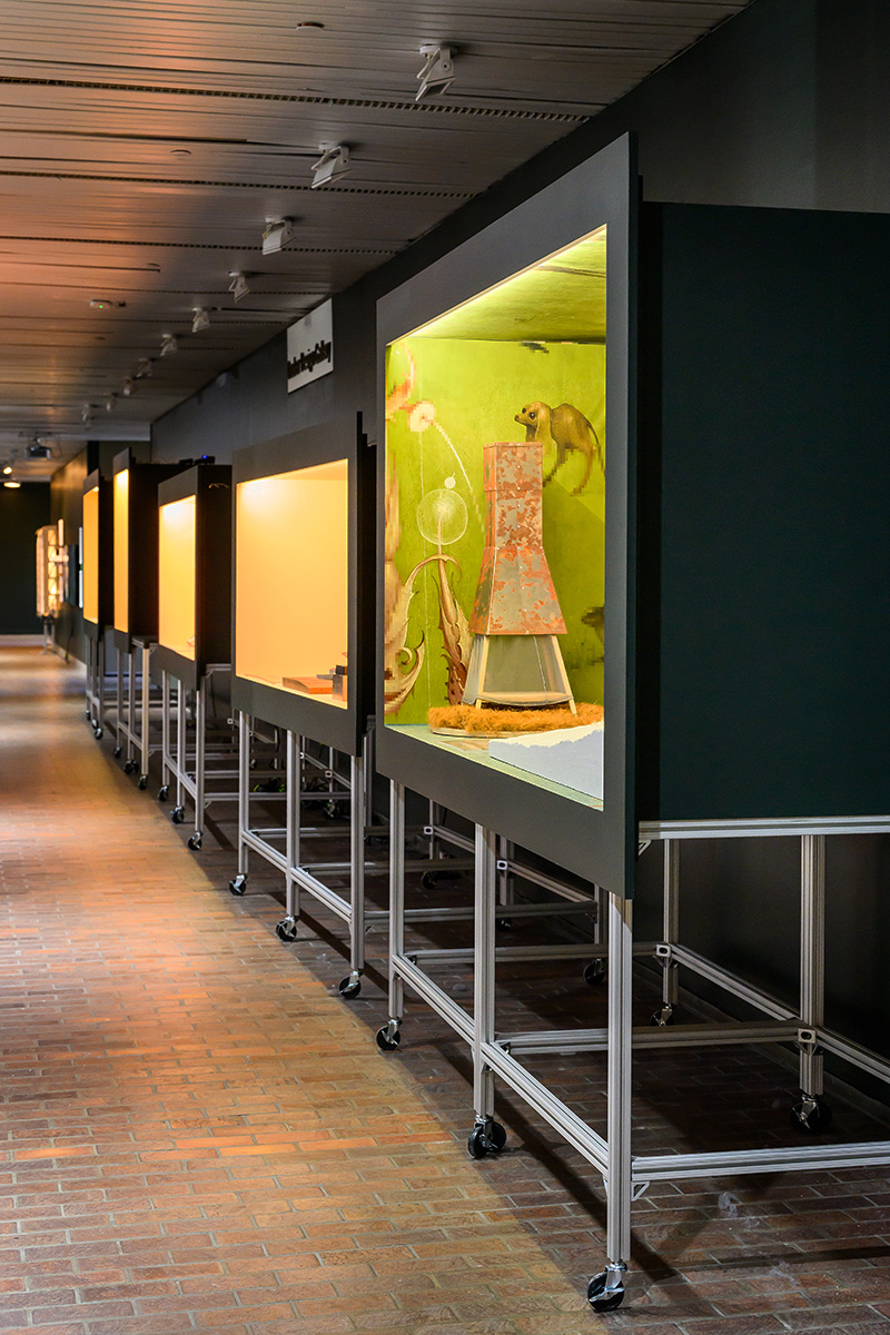 A line of lit display cases along a wall inside Druker Design Gallery.