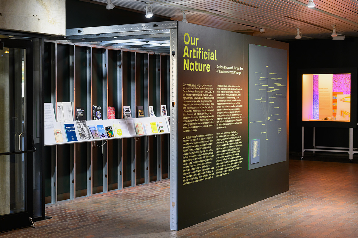 A shelf with books on display inside a temporary wall enclosure in the lobby of Gund Hall.