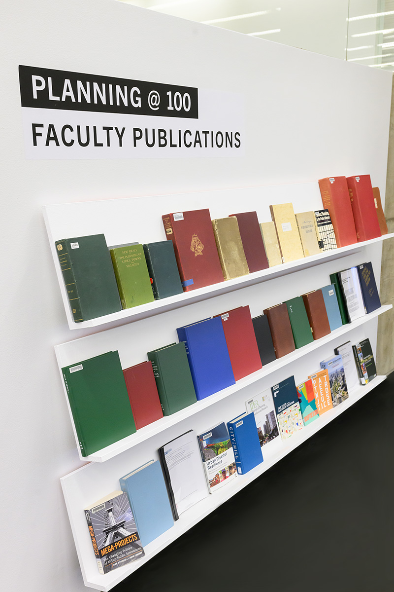 Three display shelves full of books under the heading “Planning at 100: Faculty Publications”