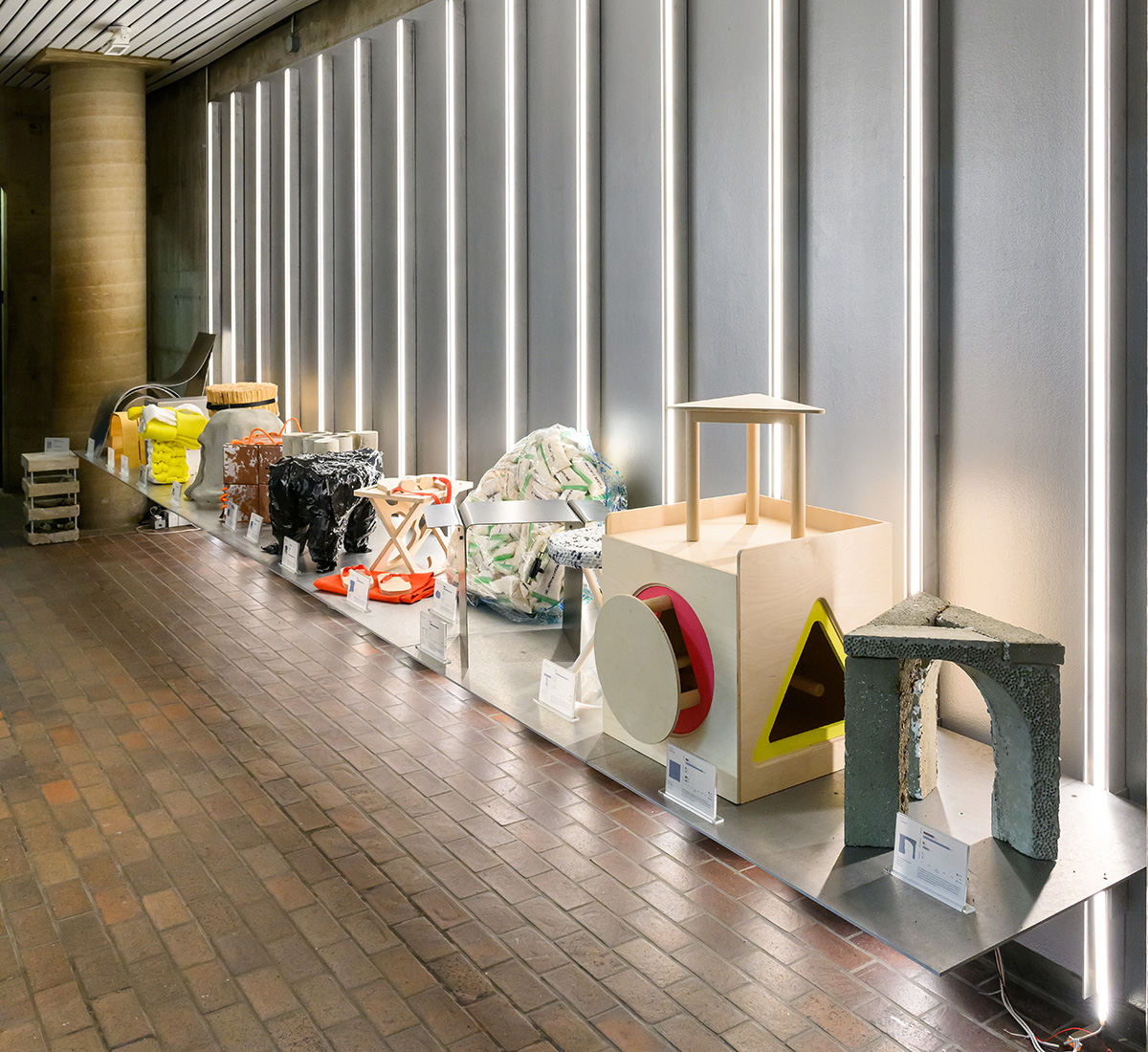 A shelf displaying a number of stools made of various materials, lit up by vertical lights on the wall behind.