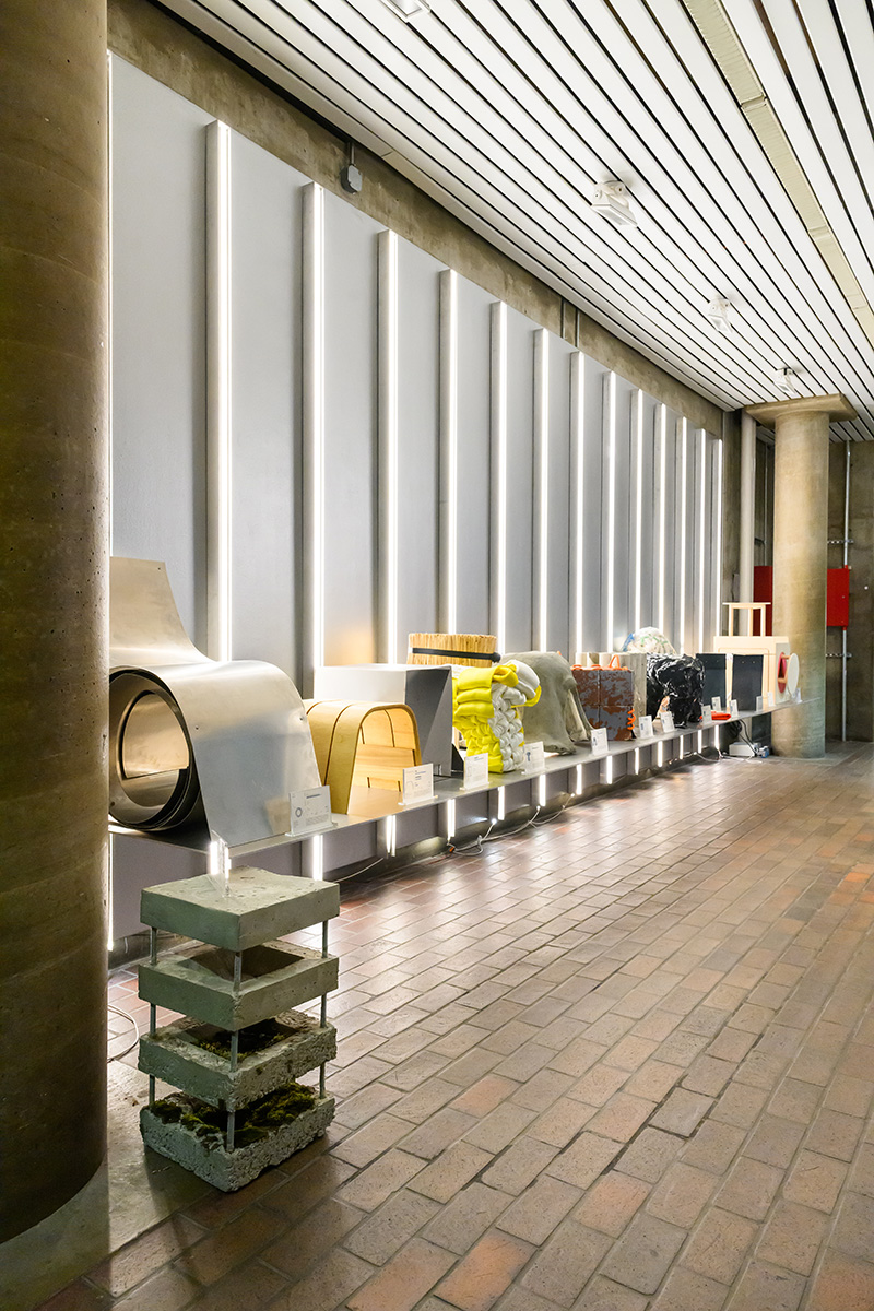 A shelf displaying a number of stools made of various materials, lit up by vertical lights on the wall behind.