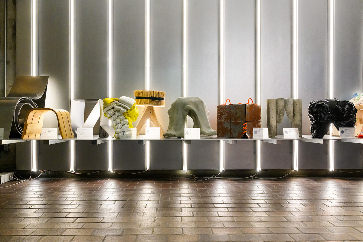 A shelf displaying a number of stools made of various materials, lit up by vertical lights on the wall behind.