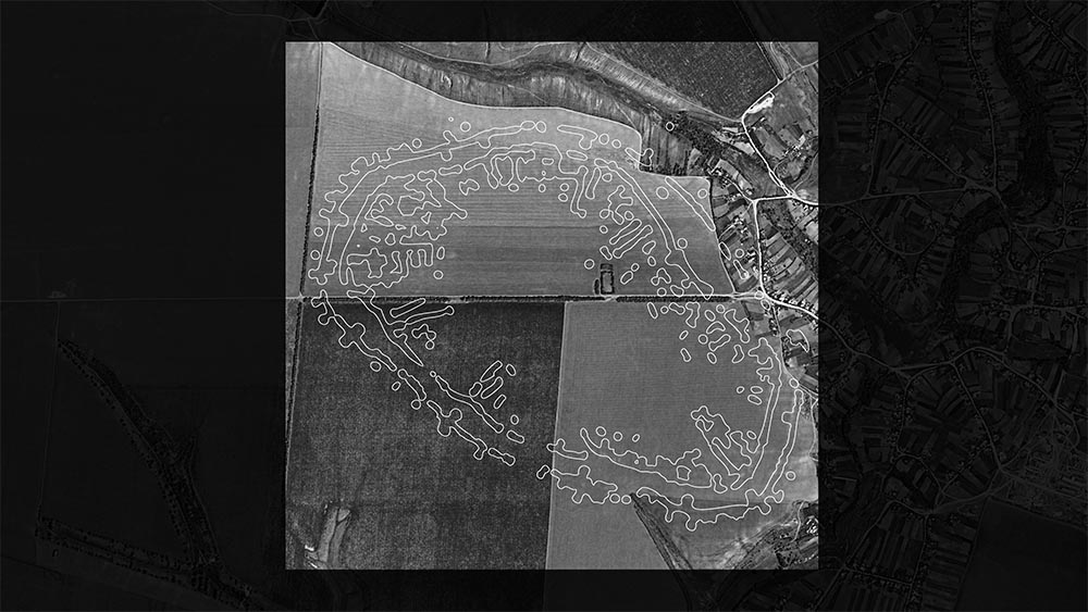 A black-and-white digital rendering of an ancient city plan overlaid on an aerial photograph of a landscape.