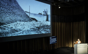 Melanie Newport speaks at "Carceral Landscapes" and shares s slide depicting a crumbling brick wall.