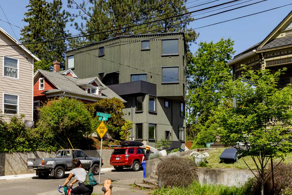 A dark green building of four stories stands on a street among single-family homes.