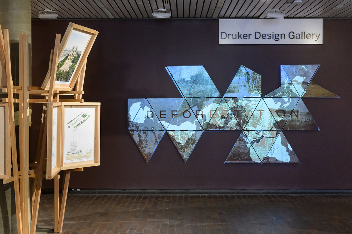 A view inside Druker Design Gallery showing a wall with a projection of trees and the word “Deforestation”.