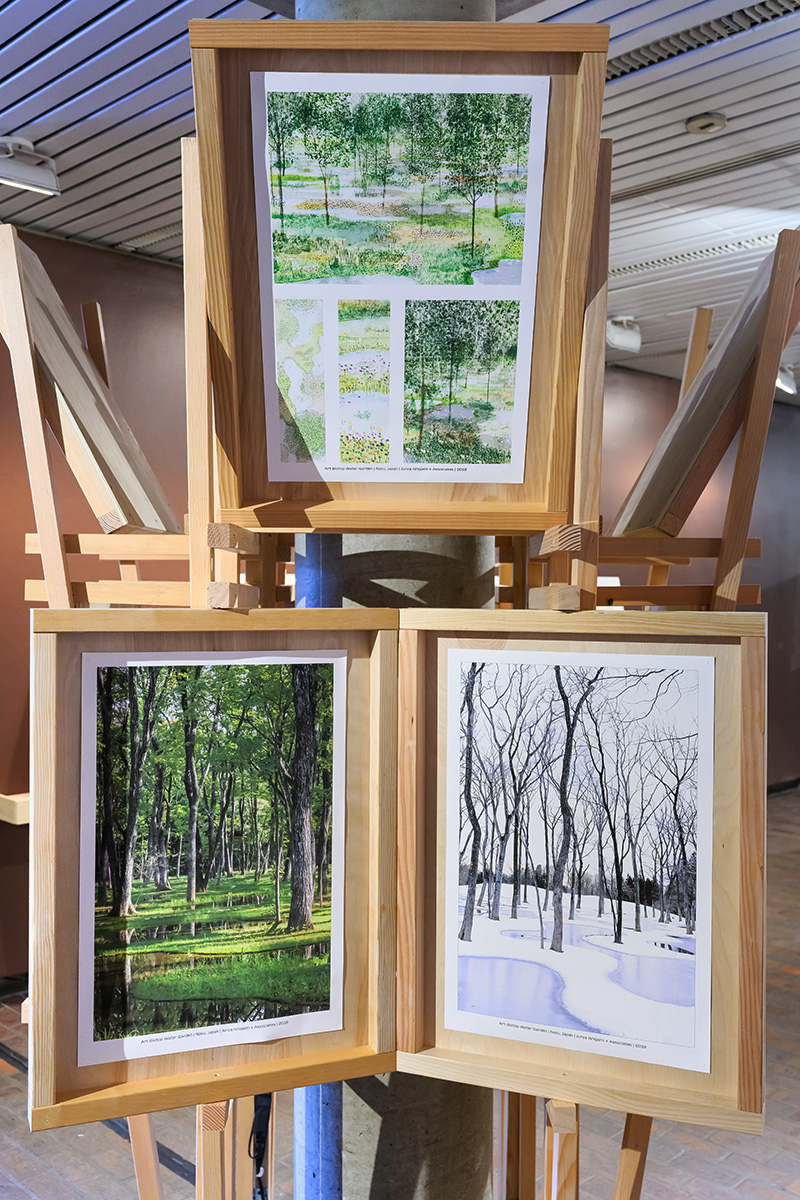 A detail of a column in Druker Design Gallery with a wooden structure built around it and three image panels of trees in a forest at different times of year.