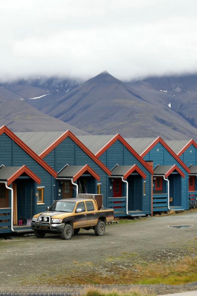 truck parked in front of red and blue cottages with mountains in background