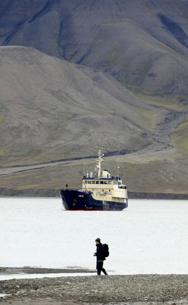 person standing on shore of lake with boat in background