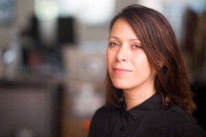 A side profile headshot of Malkit Shoshan against a blurred city background