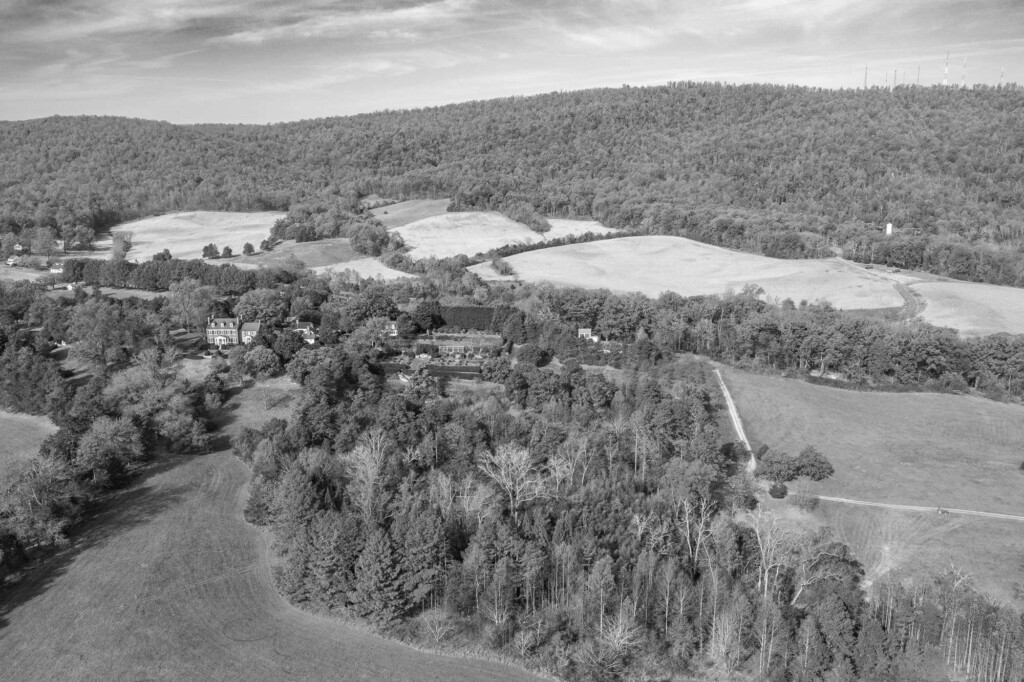 Black and white aerial image of forests and fields, with a large house to the left