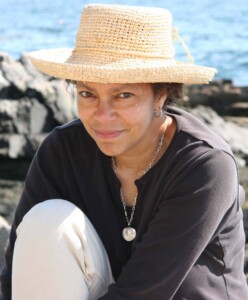 Headshot of Lauret Savoy wearing a straw hat against an ocean scene.