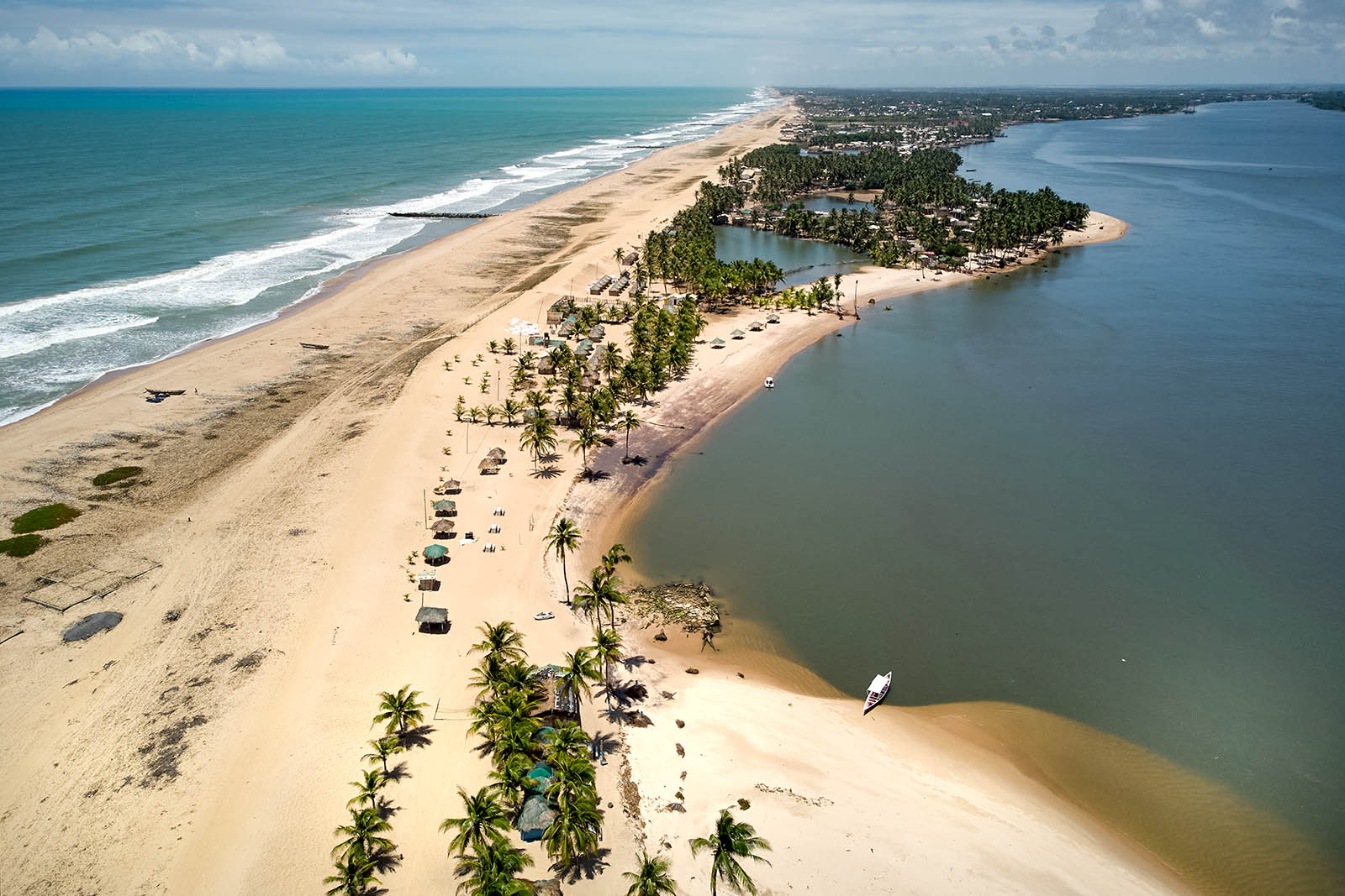 Aerial view of sandy land with river to the right and an ocean to the left.