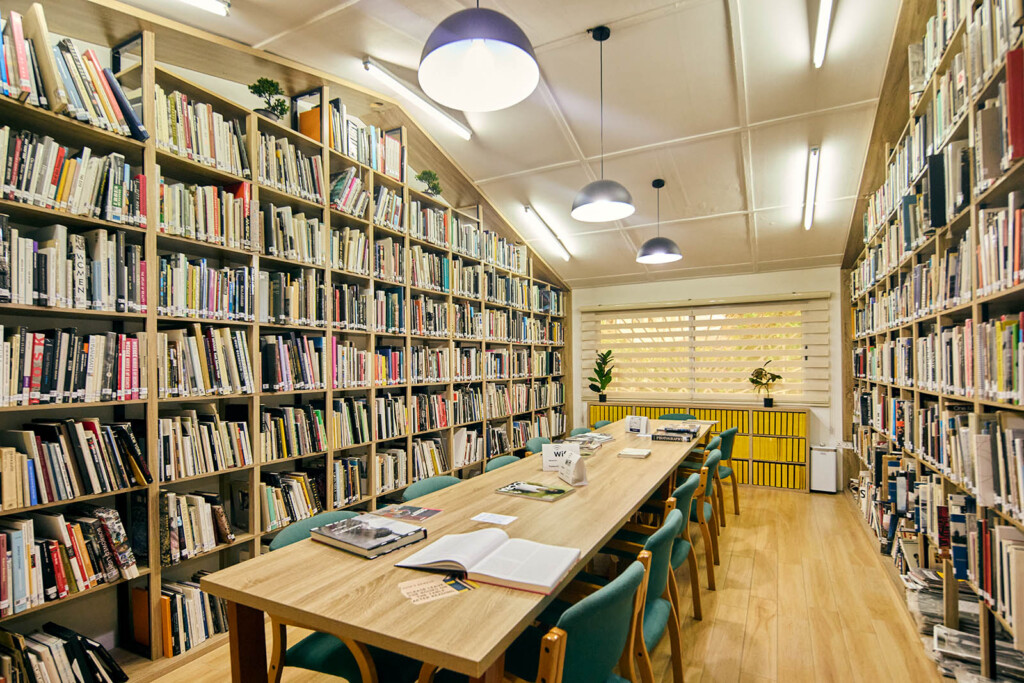 A photo of a small room with bookshelves on the left and right sides with a long table in the middle.