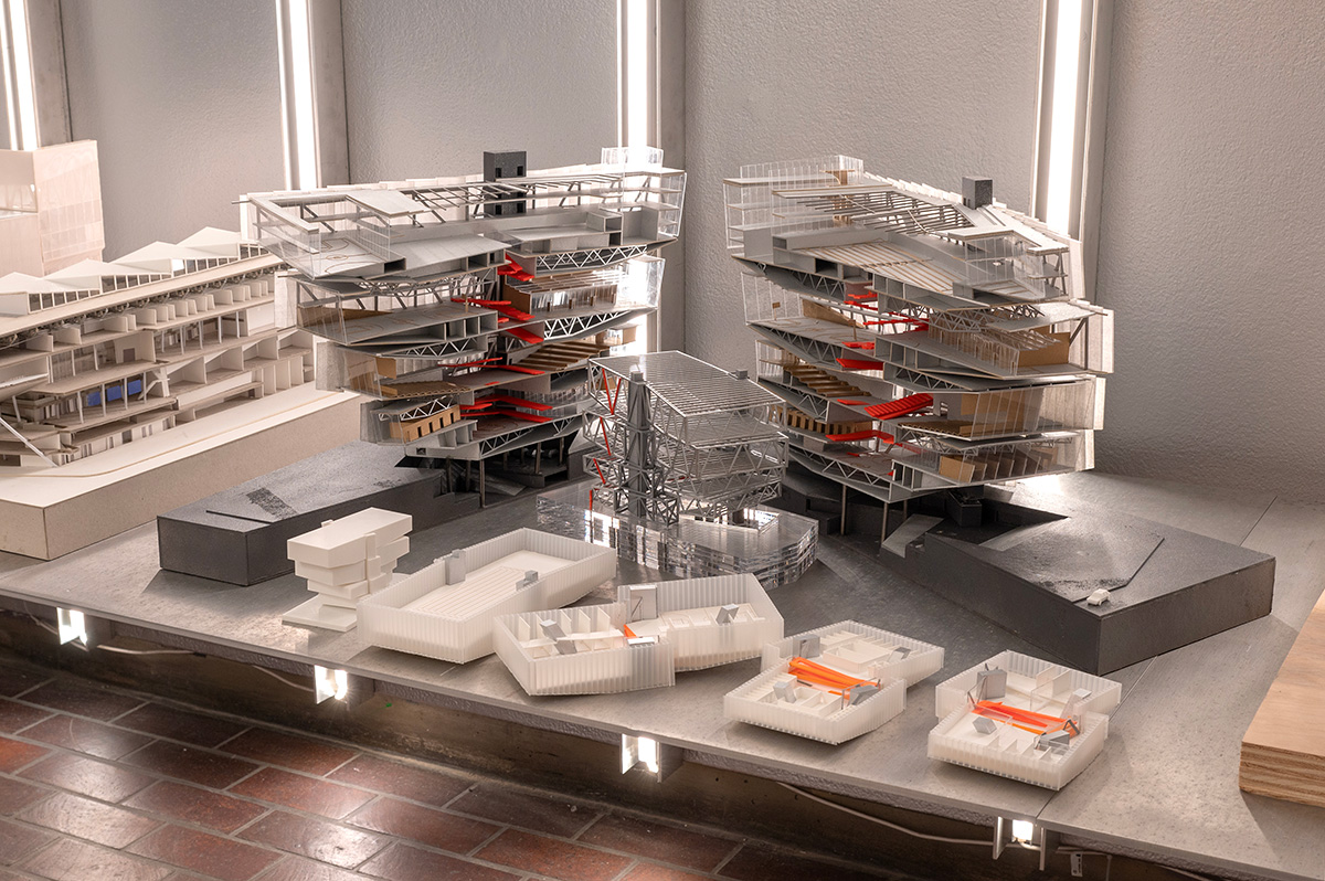 A variety of architectural models on a metal display shelf with vertical lighting behind them.