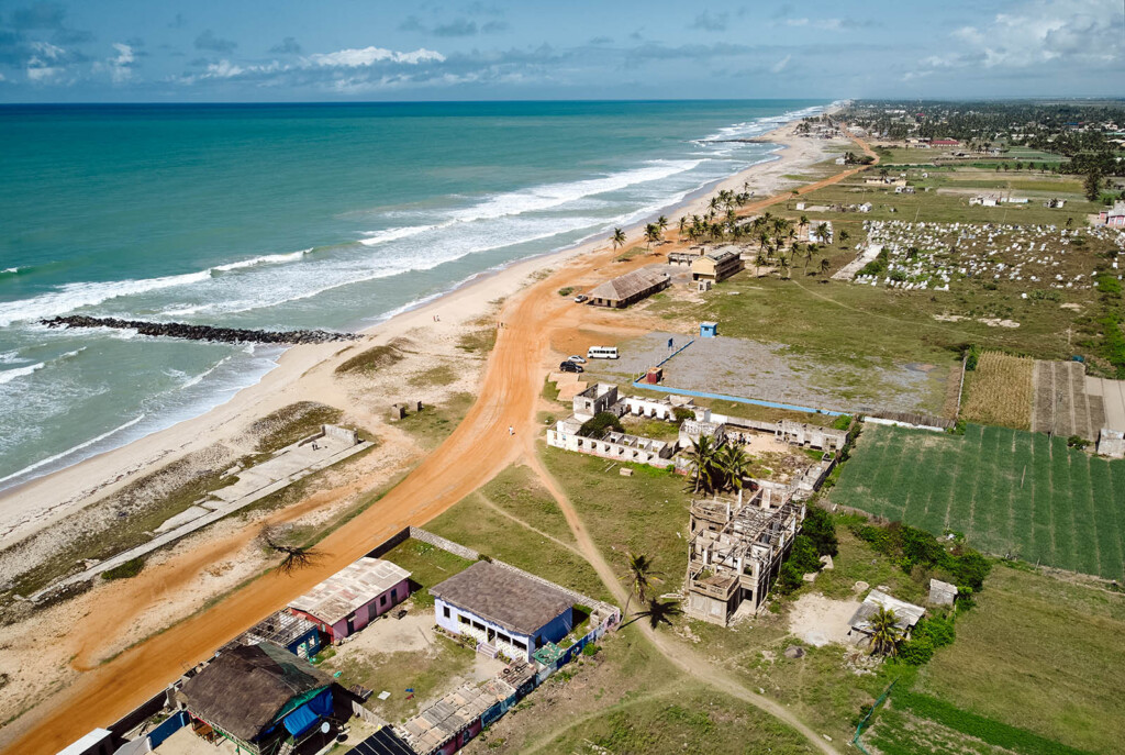 Aerial photo showing a coastline on the left and a village on the right with a gravel road running along the coast