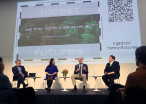 Four people sit on chairs on a low stage as part of a panel discussion. An image projected behind them says Forest Futures: Will the Forest Save us All"