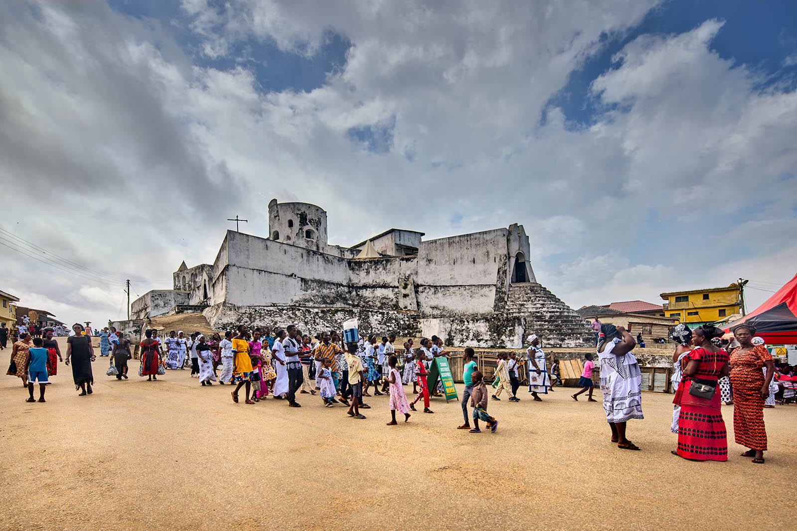 A photo of a crowd of people with a white washed fort in the background.