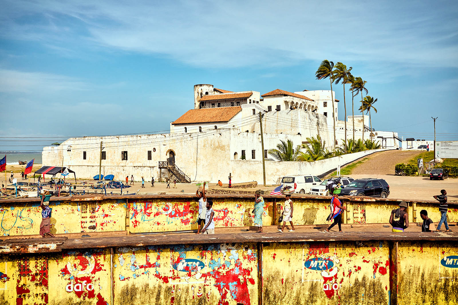 Photo of a pedestrian bridge with several people on it in the foreground and a view of a fort in the background