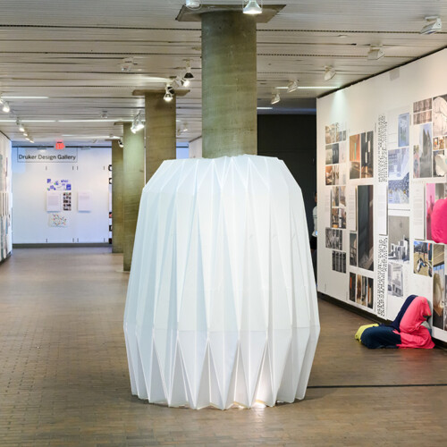 A detail of the exhibit in Druker Design Gallery, showing an accordion-style installation around a column and a large variety of images displayed on the walls.