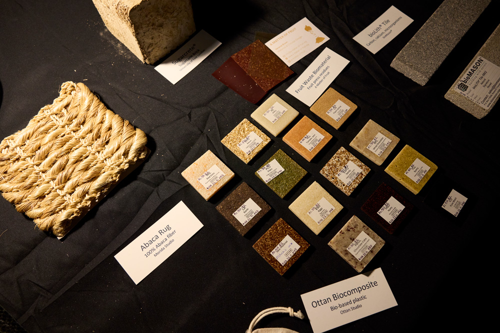 Samples of different materials including abaca fibers and squares of made of processed food waste are arrayed on a black cloth surface.