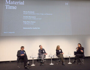 Four people sit on chairs in the auditorium of the Harvard Graduate School of Design. A woman in dark clothes on the right of the image holds a microphone and appears to be speaking.