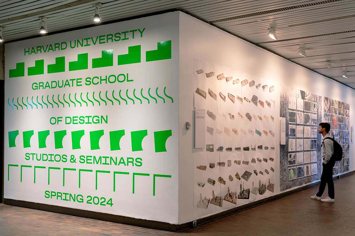 A view of the exhibit in Gund Hall, showing a variety of student work hanging on the walls.