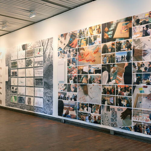 A view of the exhibit in Gund Hall, showing a variety of student work hanging on the walls.