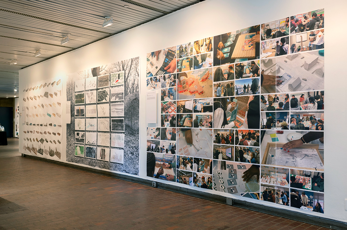 A view of the exhibit in Gund Hall, showing a variety of student work hanging on the walls.