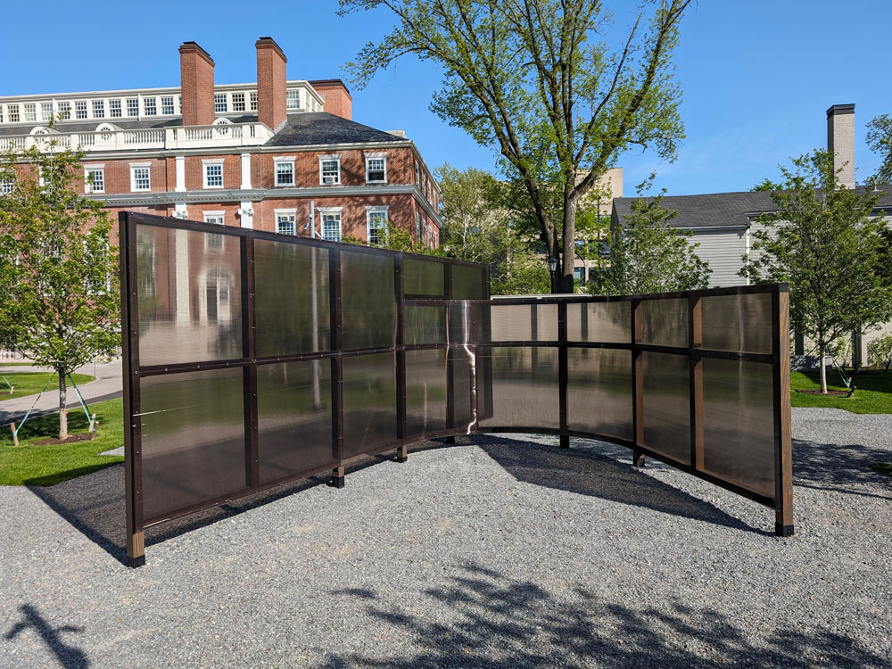 A public art installation that features on straight wall made of wood beams and plastic sheeting and a second curving wall intersecting it.