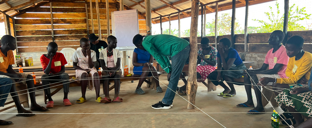 A classroom in Uganda with refugees of differing ages holding a web of string.