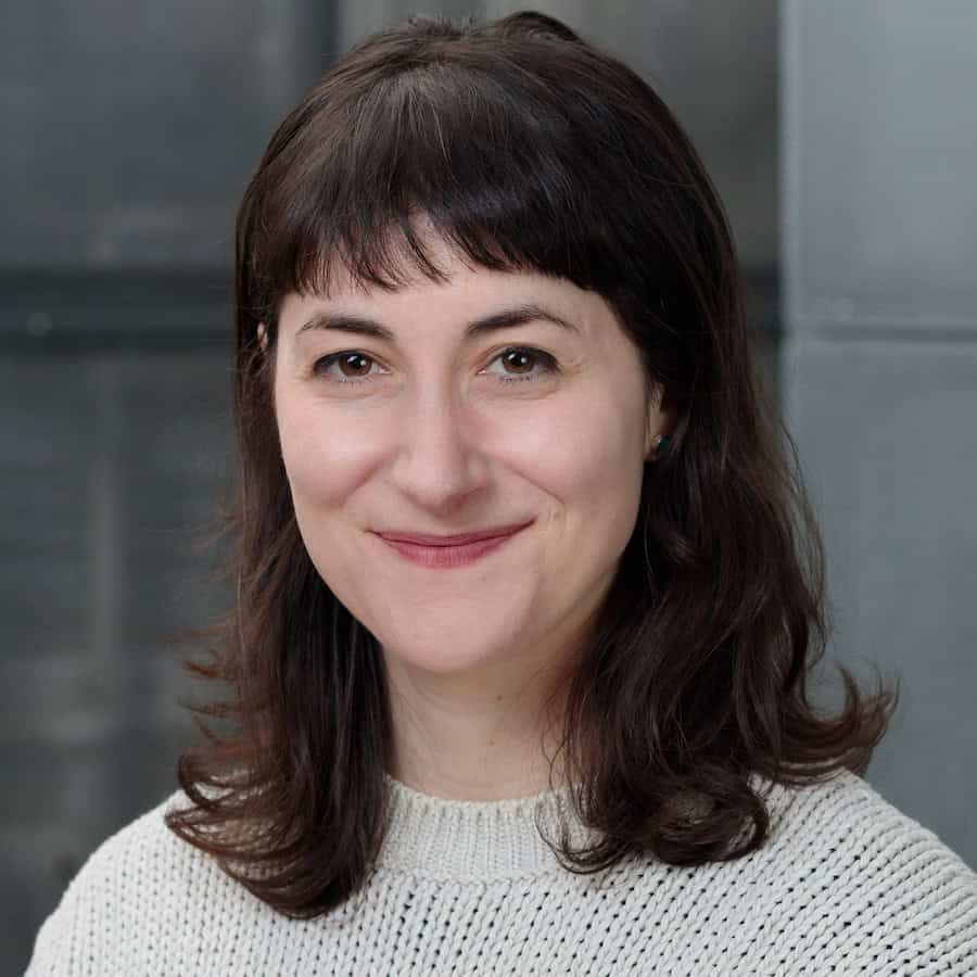 Sarah Rafson looks at the camera and smiles while wearing a cream sweater and shoulder length brown hair.