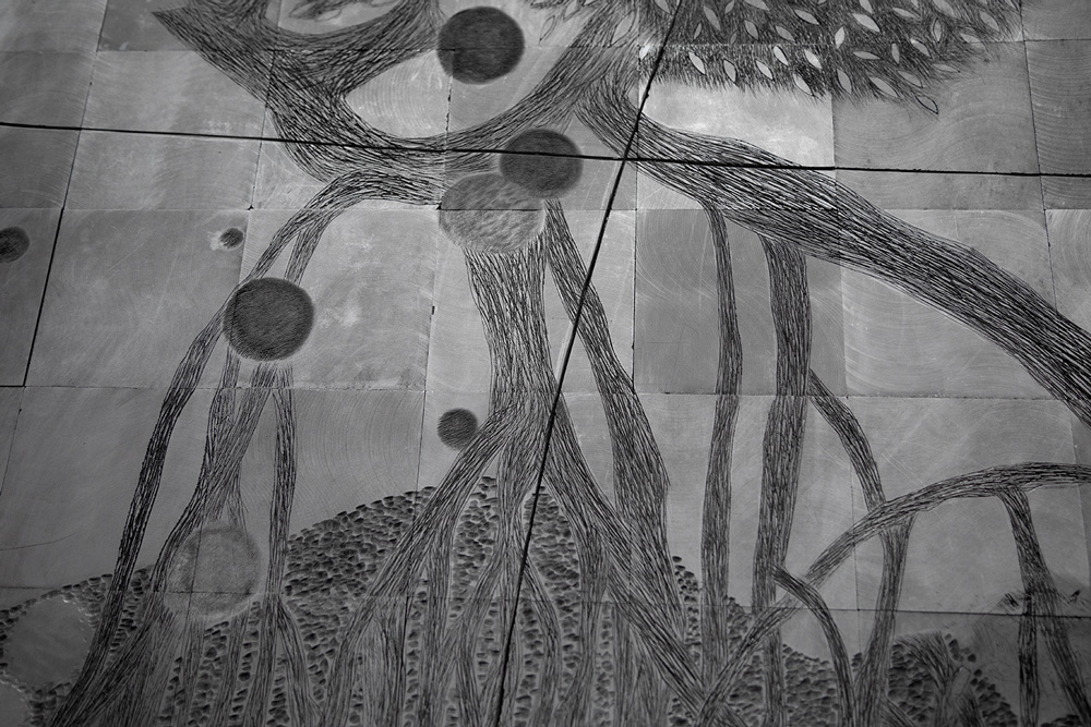 A black-and-white photograph showing an abstract composition resembling a tree's root system etched into metal panels that are arranged in a grid.