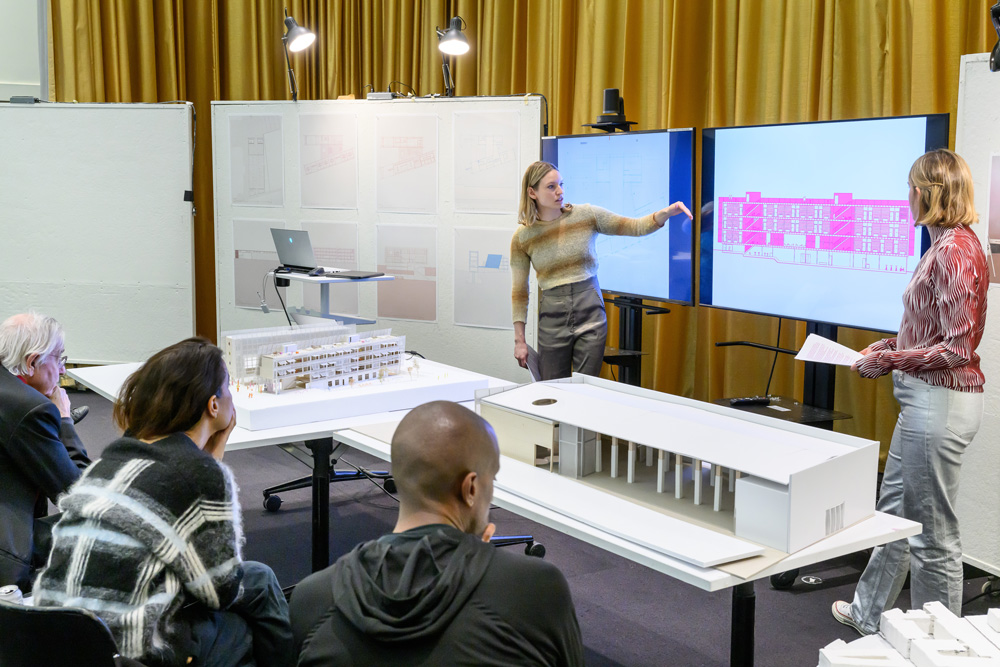 Two students present drawings and architectural models in a final review of an option studio.