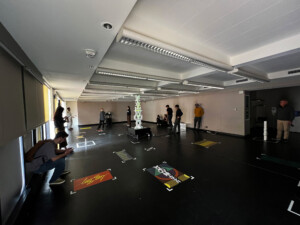 A photograph of the mediums domain open projects featuring a pillar sculpture in the center of a large open room on the floor of which is projected a number of rectangular graphics.
