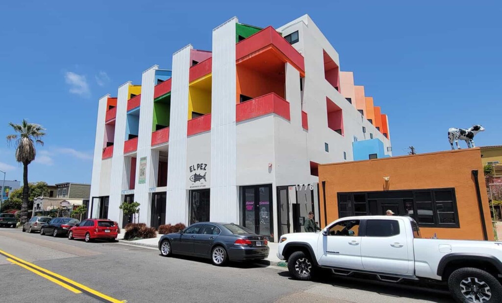 Outdoor photograph of vibrant and colorful building with cars parked outside.