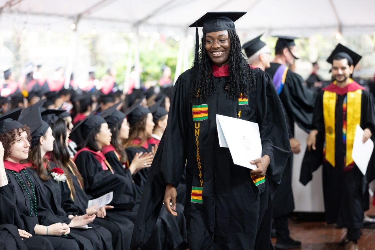 A graduate with a diploma walks in front of other seated graduates