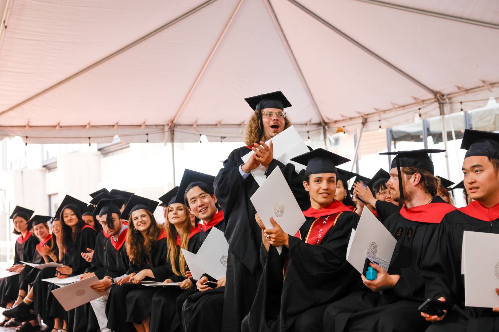 Graduates in regalia and holding diplomas cheer